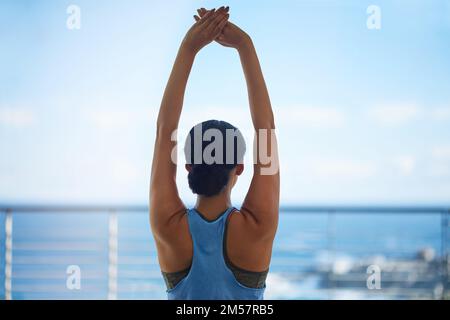 Faire de l'exercice avec une vue. Vue arrière photo d'une jeune femme qui s'étire face à une vue sur l'océan. Banque D'Images