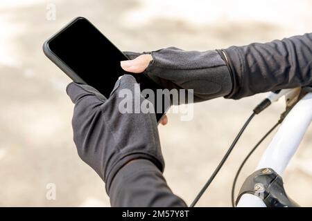 Femme tenant un smartphone avec écran noir tout en étant assise sur son vélo dans le parc. Écran noir pour l'espace de copie Banque D'Images