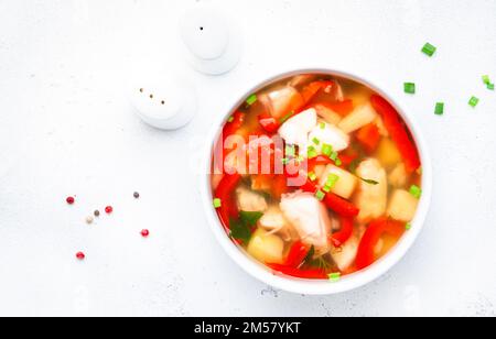 Soupe de poisson avec truite, paprika rouge, pommes de terre, tomates et persil dans un bol à soupe en céramique sur fond de table blanc, vue du dessus Banque D'Images