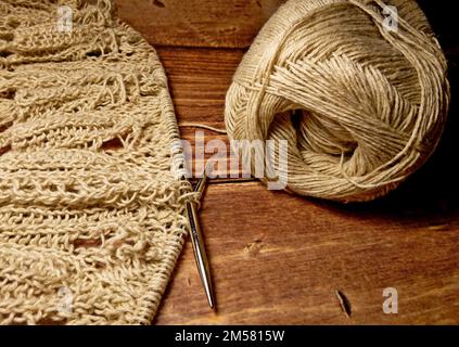Nappe ajourée dans le processus de tricotage. Aiguilles à tricoter, boucles sur aiguilles à tricoter, tissu tricoté, pelote de fil, coton grossier et lin Banque D'Images