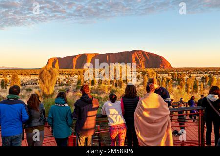 Les visiteurs sur une plateforme d'observation voient Uluru (Ayers Rock) rougeoyer à l'aube dans le parc national d'Uluru-Kata Tjuta, Territoire du Nord, Australie. Banque D'Images