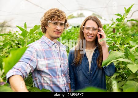 Agronomes en lunettes de protection prenant un selfie en serre Banque D'Images