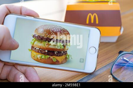 Un homme consulte le site Web de McDonald's pour obtenir des informations sur un hamburger avant de déjeuner. Grande boîte Mac sur la table du restaurant McDonald's. Banque D'Images