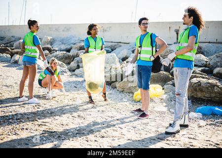 Les gens nettoyant la plage, les volontaires collectant les déchets sur la côte, les jeunes amis de la génération z travaillant en équipe conscients de la pollution pro Banque D'Images