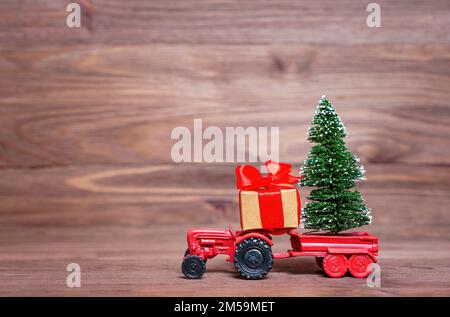Figurine tracteur miniature avec un arbre de Noël miniature placé dans le chariot et une grande boîte cadeau isolée sur un fond en bois sombre. Banque D'Images