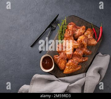 Ailes de poulet rôties barbecue avec sauce et herbes fraîches sur un panneau de bois sur fond sombre. Le concept des en-cas pour le menu. Vue de dessus et copie de la flèche Banque D'Images