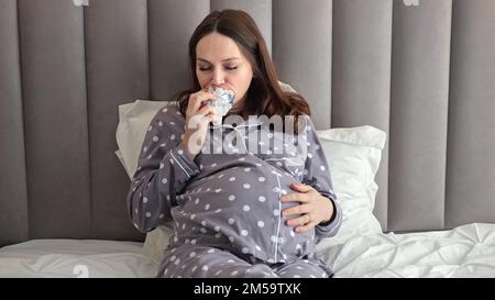 La femme enceinte aime manger un sandwich sain dans un lit double Banque D'Images