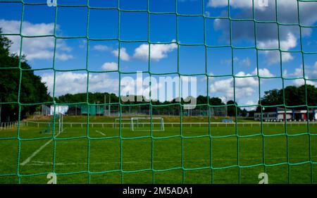 Vue à travers un filet de but de football sur un terrain de sport déserté avec pelouse verte fraîche et ciel bleu (variante A) Banque D'Images