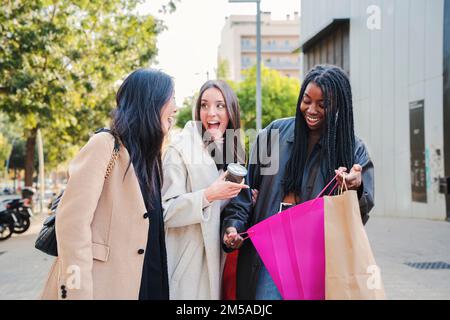 Groupe de jeunes femmes heureux multiethniques suprised regardant à l'intérieur d'un sac de shopping à l'extérieur. Trois filles de shopping surpris par leurs nouveaux vêtements achetés le jour de la vente. Concept de consommables. Photo de haute qualité Banque D'Images