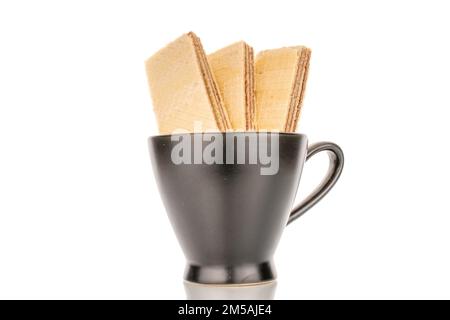 Trois gaufrettes au chocolat dans une tasse en céramique noire, en gros plan, isolées sur un fond blanc. Banque D'Images