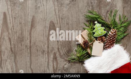 Noël présente dans la chaussette rouge du Père Noël avec des branches de conifères naturelles comme décoration. Vue de dessus, plat sur une table en bois. Cadeaux de la nouvelle année. Bannière Banque D'Images