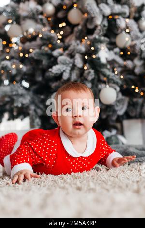 Petite fille enfant près de l'arbre de Noël dans un costume rouge Banque D'Images