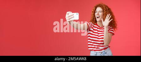 Joyeuse amicale énergique belle-look redhead maurily-cheveux femelle envoyer bonjour en agitant la paume sourire blogueur largement enregistrer vie flux de discussion fans Banque D'Images