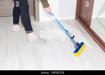 Une femme lave le sol stratifié dans l'appartement avec une vadrouille. Nettoyage de la maison. Banque D'Images