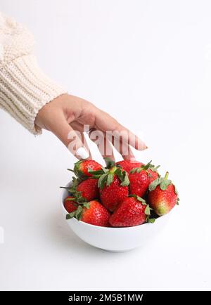 Un cliché vertical d'une main cueillant des fraises dans un bol blanc sur une surface blanche Banque D'Images