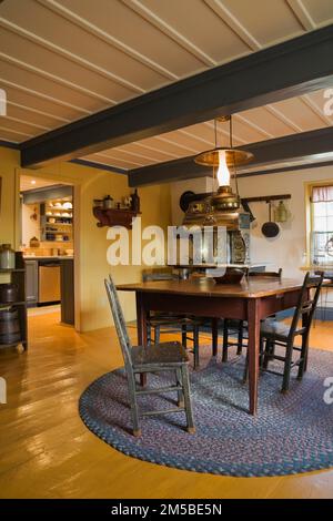 Table en bois antique et chaises sur le dessus du tapis ovale tissé dans la salle à manger avec de larges planches peintes en jaune à l'intérieur de la vieille maison de style 1722 du régime français. Banque D'Images