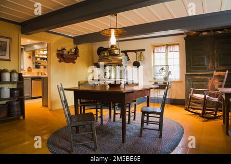 Table en bois antique et chaises sur le dessus du tapis ovale tissé dans la salle à manger avec de larges planches peintes en jaune à l'intérieur de la vieille maison de style 1722 du régime français. Banque D'Images