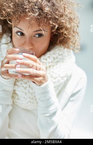 Rien ne dit l'hiver comme un verre de lait chaud. une jeune femme vêtue de vêtements chauds buvant un verre de lait. Banque D'Images
