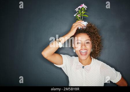 Shes aller pot. Portrait studio d'une jeune femme attrayante tenant une fleur sur la tête contre un fond gris. Banque D'Images