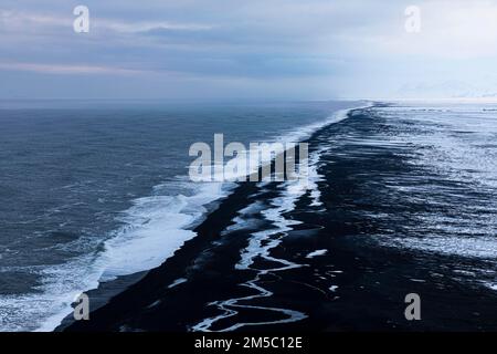 Vagues blanches mourantes et surfaces glacées sur la plage de galets noirs Skogarsandur, près de Dyrholaey, Sudurland, Islande Banque D'Images