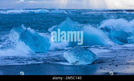 Vagues se brisant sur des icebergs sur la plage noire de Breidamerkursandur, près de Joekullsarlon, Sudurland, Islande Banque D'Images