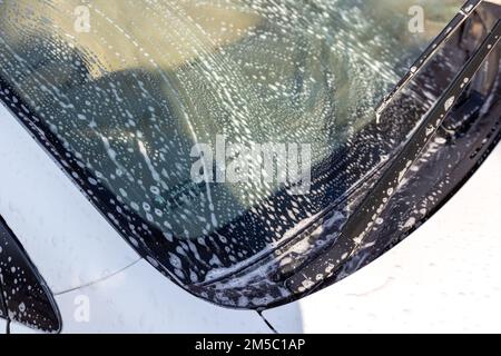 Voiture blanche recouverte de mousse de lavage et de savon. Concept de lavage de voiture. Banque D'Images