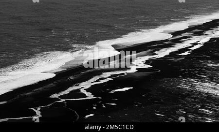 Vagues blanches mourantes et surfaces glacées sur la plage de galets noirs Skogarsandur, près de Dyrholaey, photo noir et blanc, Sudurland, Islande Banque D'Images