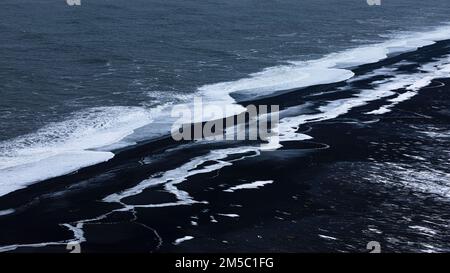 Vagues blanches mourantes et surfaces glacées sur la plage de galets noirs Skogarsandur, près de Dyrholaey, Sudurland, Islande Banque D'Images