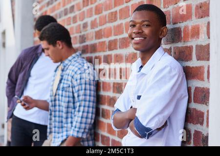 J'ai fait quelques amis cool à l'université. Portrait d'un étudiant universitaire sur le campus avec ses amis en arrière-plan. Banque D'Images