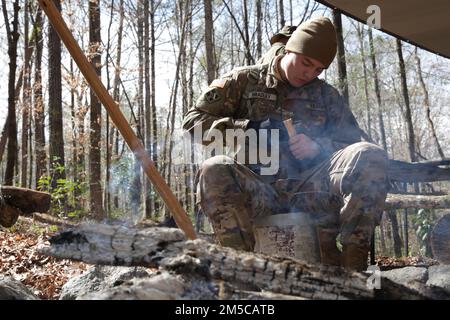 L'Adjudant Joshua Bradley, futur étudiant en vol inscrit au cours d'entraînement survie, évasion, résistance et évasion, blanchit un morceau de bois avec un couteau de combat pendant l'entraînement de survie sur le terrain à fort Rucker, Alabama, 1 mars 2022. « C'est un cours très divertissant. C'est très essayer, mais je m'amuse bien. C'est comme le camping de l'Armée de terre », a déclaré Bradley au sujet du cours SERE. Banque D'Images