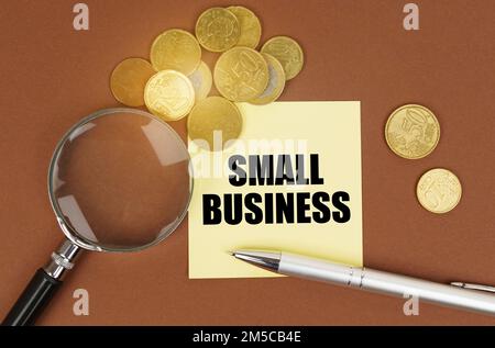 Concept d'entreprise. Sur une surface marron sont des pièces de monnaie, un stylo, une loupe et des autocollants avec l'inscription - petite entreprise Banque D'Images