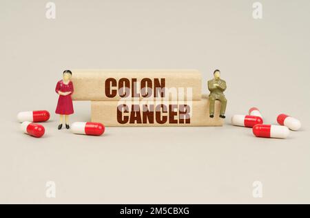 Concept médical. À côté des figurines miniatures des gens sont des comprimés et des blocs de bois avec l'inscription - CANCER DU CÔLON Banque D'Images