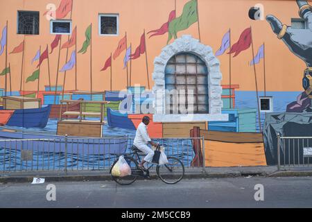 Un cycliste passe devant une peinture murale colorée à Sassoon Docks, Colaba, Mumbai, Inde, représentant des bateaux de pêche ancrés dans les Docks Banque D'Images