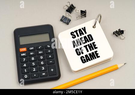 Concept d'entreprise. Sur une surface grise, une calculatrice, un crayon et un bloc-notes avec inscription - restez en tête du jeu Banque D'Images