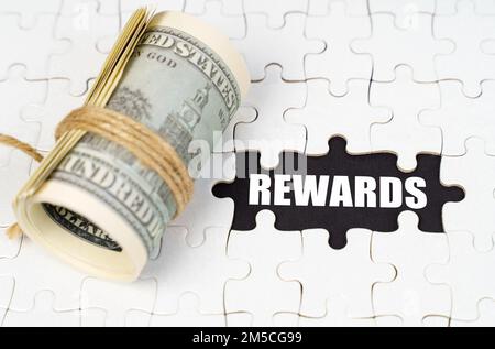 Concept d'entreprise. Les dollars se trouvent sur des puzzles blancs, sur une surface noire il y a une inscription - RÉCOMPENSES Banque D'Images