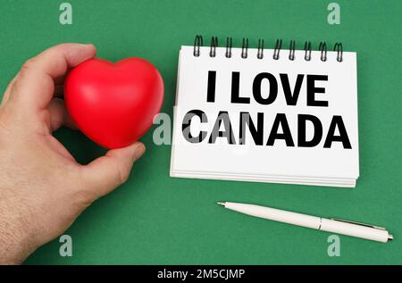 Sur la surface verte se trouvent un stylo, un bloc-notes avec l'inscription - j'aime le Canada. Un homme a un cœur dans ses mains. Banque D'Images