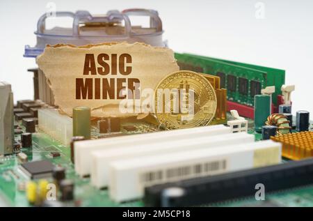 Crypto - concept d'entreprise. Sur la carte mère se trouve une pièce en bitcoin et un panneau en carton avec l'inscription - ASIC Miner Banque D'Images