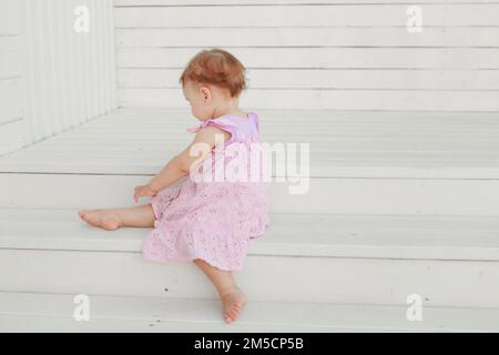 Une fille d'apparence européenne dans une robe rose est assise sur une échelle blanche, magnifiquement comme une ballerine. Bel enfant. Une famille heureuse. Gymnastique, sports et danse pour les enfants. Photo de haute qualité Banque D'Images