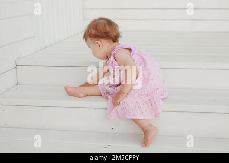 Une fille d'apparence européenne dans une robe rose est assise sur une échelle blanche, magnifiquement comme une ballerine. Bel enfant. Une famille heureuse. Gymnastique, sports et danse pour les enfants. Photo de haute qualité Banque D'Images