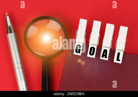 Concept d'entreprise. Sur la surface rouge il y a une loupe, un bloc-notes et des épingles à linge avec l'inscription - BUT Banque D'Images