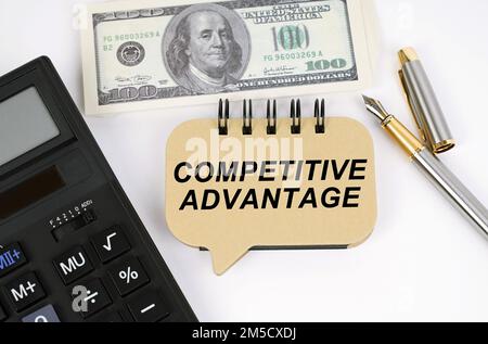 Concept d'entreprise. Sur une surface blanche, une calculatrice, des dollars, un stylo et un signe avec l'inscription - AVANTAGE CONCURRENTIEL Banque D'Images