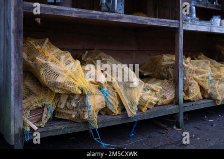 De petits morceaux de bois de chauffage, enveloppés dans un filet de nylon jaune, sont mis en vente dans un rack métallique. Bâtonnets ou bois facilement combustibles utilisés pour faire feu Banque D'Images