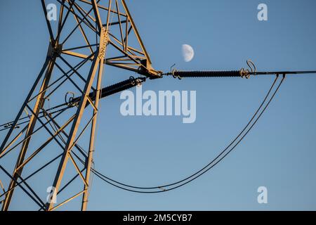 Un faible angle d'une tour de câble haute tension contre la demi-lune dans le ciel bleu Banque D'Images