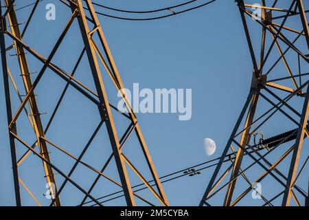 Un faible angle d'une tour de câble haute tension contre la demi-lune dans le ciel bleu Banque D'Images