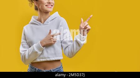 Femme méconnaissable indiquant la bonne direction avec les index à l'intérieur. Rogner la vue de la femme, en pointant vers l'extérieur avec des mains propres, souriant, isolé sur fond orange studio. Concept de gestuelle. Banque D'Images