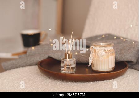 Parfum liquide maison en bouteille de verre et bâtonnets de bambou avec bougie allumée sur lumières de Noël phosphorescentes dans la chambre à coucher. Saison des vacances d'hiver. Banque D'Images