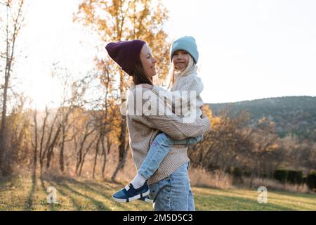 Sourire bonne mère tenant bébé fille porter des vêtements décontractés dans le parc d'automne extérieur. Contenu familial. Maternité. Banque D'Images