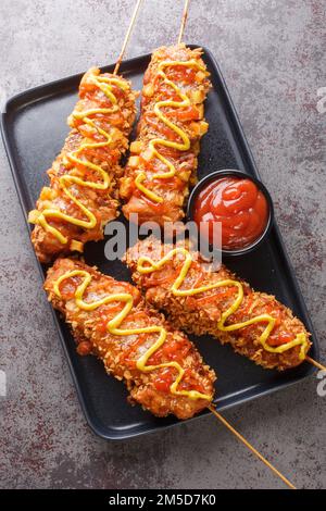 Les chiens de maïs coréens sont des hot dogs enrobés d'une pâte, puis frits en profondeur et finis avec de la moutarde et du ketchup sur l'assiette de la table. Verti Banque D'Images