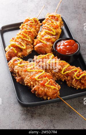 Les chiens de maïs coréens sont des hot dogs enrobés d'une pâte, puis frits en profondeur et finis avec de la moutarde et du ketchup sur l'assiette de la table. Verti Banque D'Images