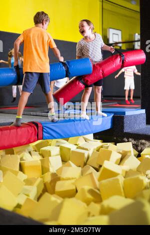 Enfants excités garçon et fille ayant la lutte drôle par des rondins gonflables tout en célébrant l'anniversaire dans le centre de sport de loisirs pour les enfants Banque D'Images